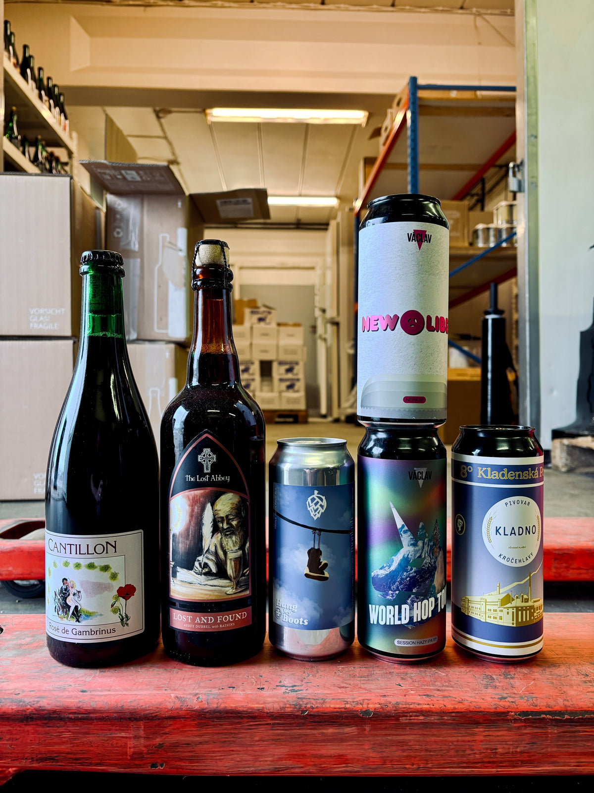 September 2026 monthly box on a red pallet in a warehouse: Cantillon Rosé de Gambrinus, Lost Abbey Lost and Found, Monkish Hang My Boots, Pivo Václav New Libeň and World Hop Tour, and Kladno Kladenská Poldi 8°